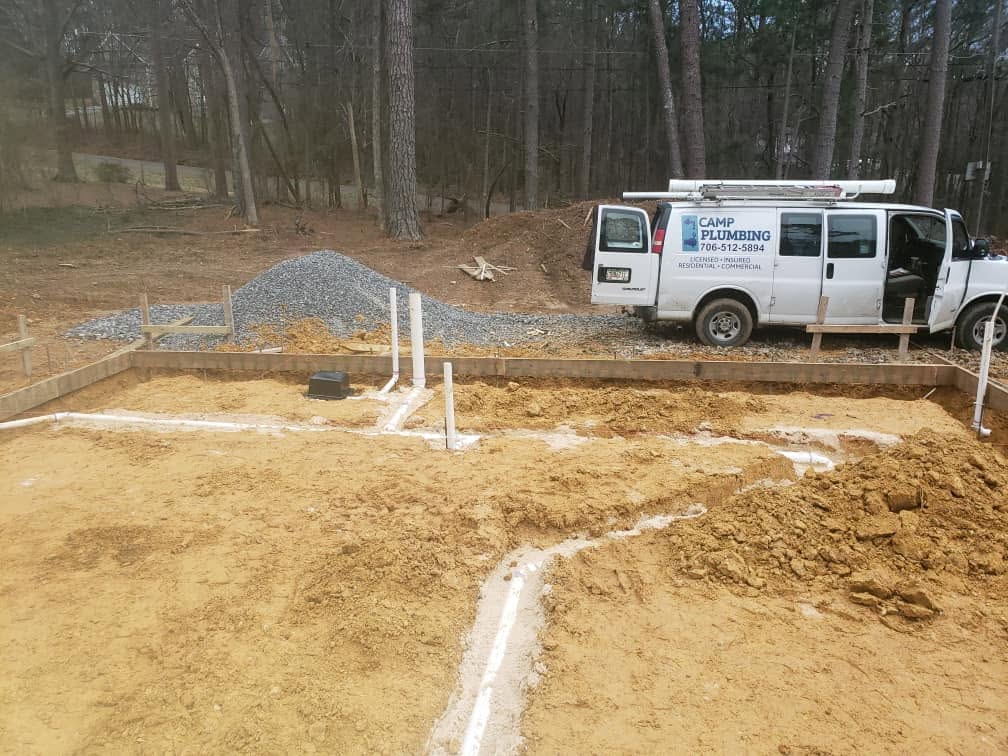 Foundation pad with underground plumbing stub-ups and the Camp Plumbing van parked beside the site