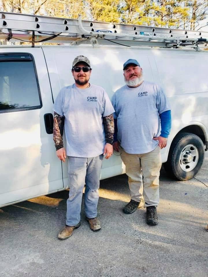 Two Camp Plumbing plumbers standing together beside the company service van on a job site