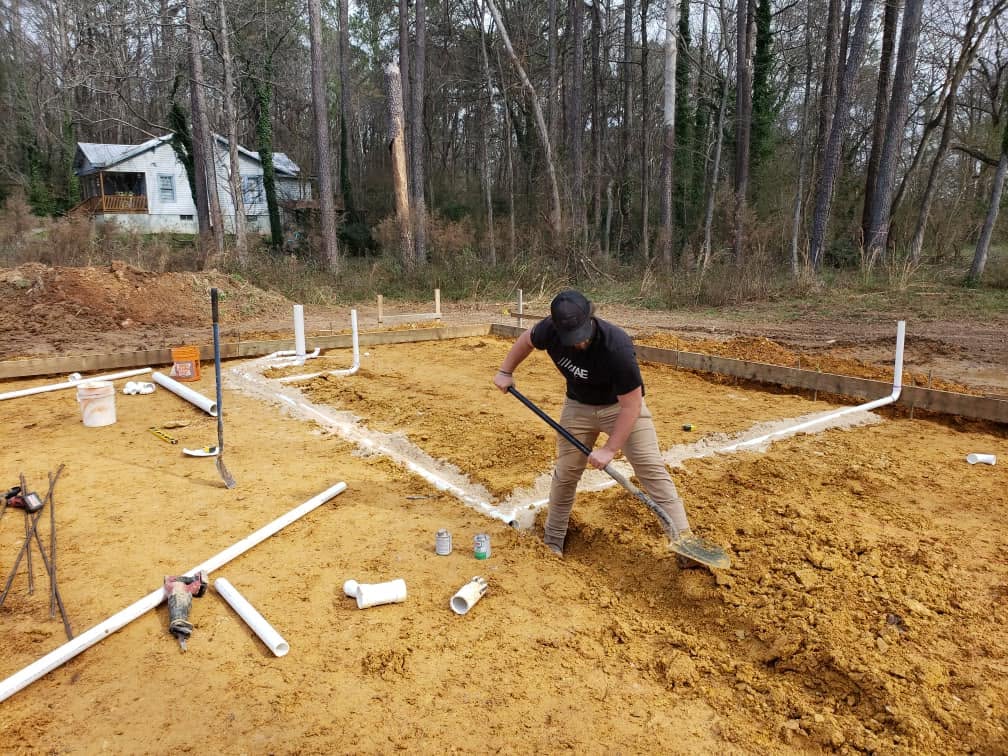 Camp Plumbing worker shoveling soil over newly installed underground PVC piping
