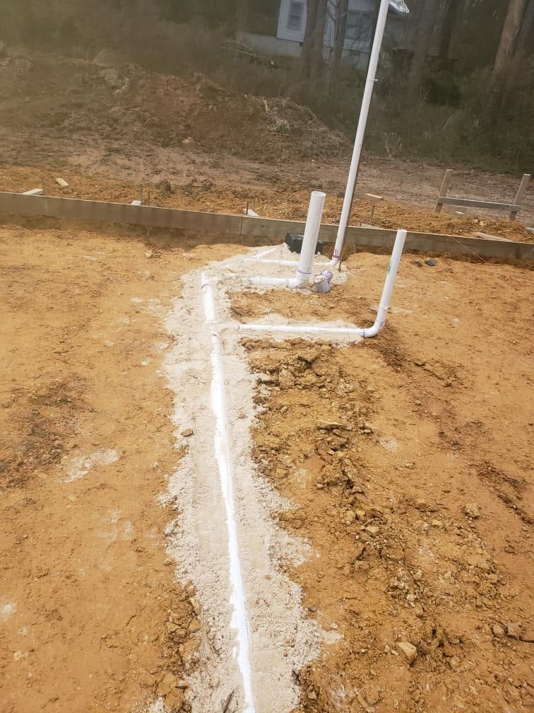 Close view of PVC drain piping and vent stack bedded in sand before a slab pour