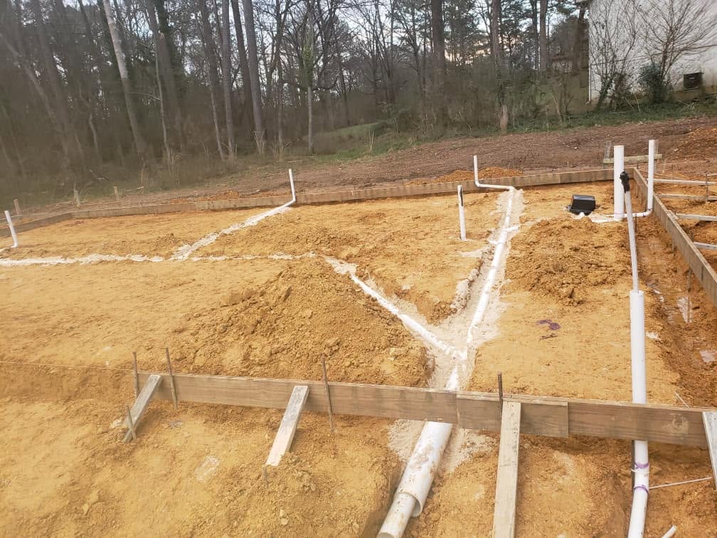 Underground drain lines laid out in graded sand inside a new home foundation form
