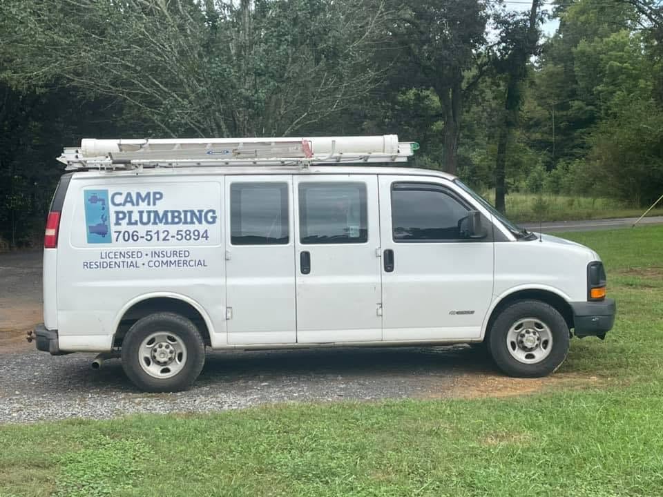 The white Camp Plumbing service van with company name, phone number, and licensed, insured, residential and commercial lettering on the side